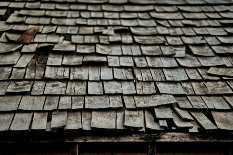 A homeowner inspecting worn shingles and water stains beneath a residential roof.